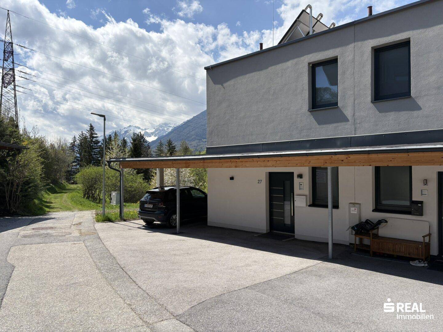 Vorderansicht des modernen Hauses mit Carport und Zufahrt in alpiner Umgebung.