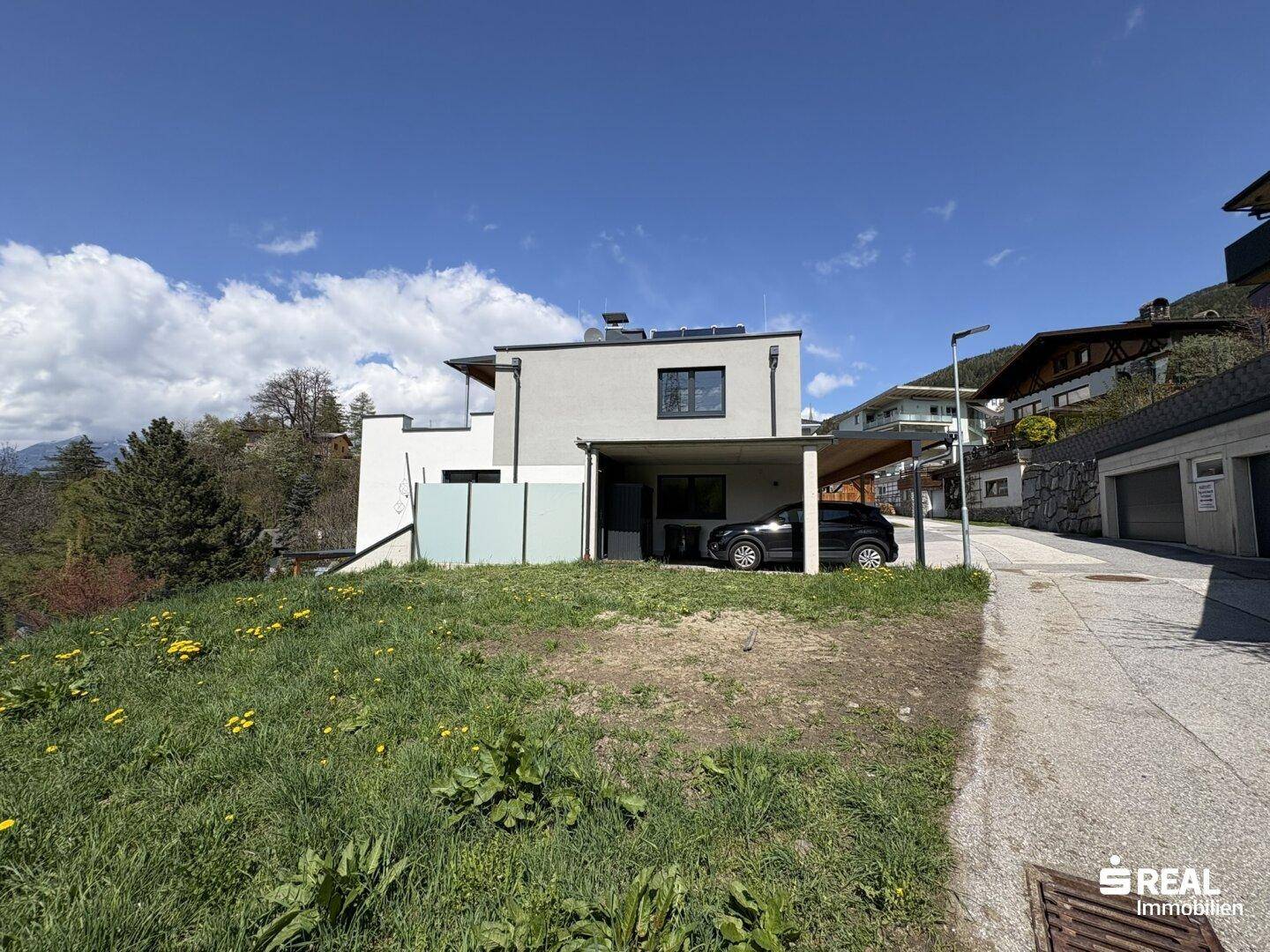 Gesamtansicht des modernen Hauses mit Carport und Hanglage unter blauem Himmel.