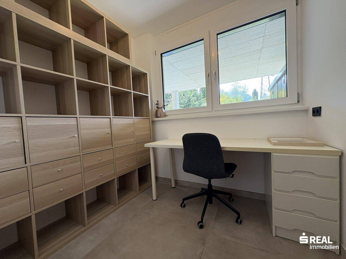Helles Arbeitszimmer mit großem Fenster, Schreibtisch und praktischen Regalsystemen.