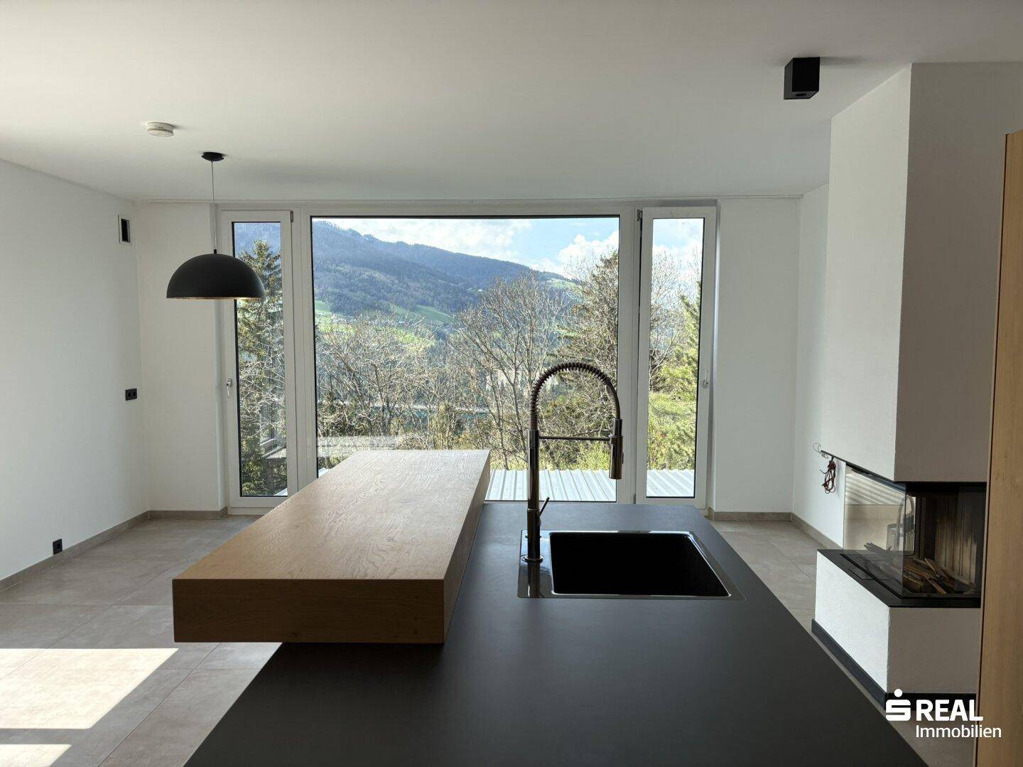 Lichtdurchfluteter Wohnbereich mit offener Küche, Kamin und Panoramafenstern mit Bergblick.