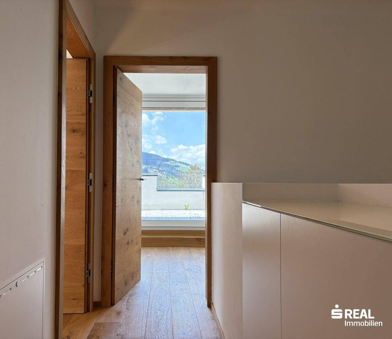 Heller Flur mit Holzboden und Zugang zu einem Zimmer mit Bergblick.