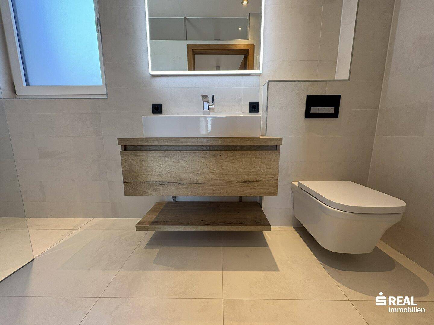 Modernes Badezimmer mit schwebendem Waschtisch, Wand-WC und großem Spiegel.