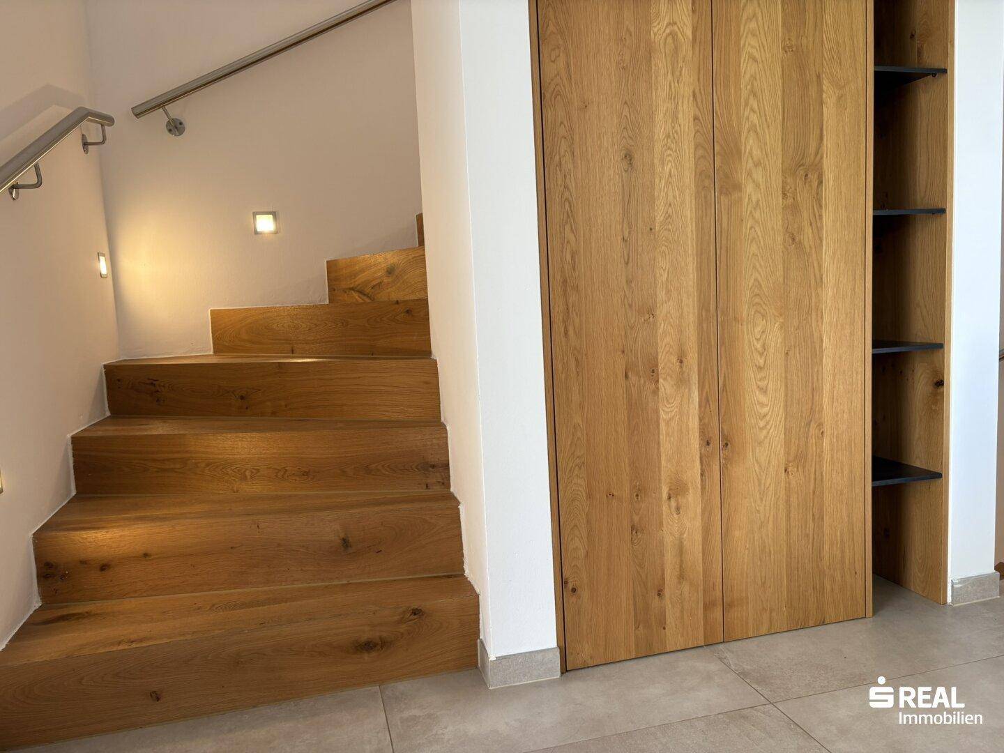 Holztreppe mit integrierten Schränken und modernem Handlauf im Flurbereich.