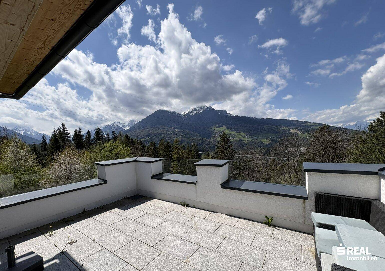 Sonniger Dachterrassenbereich mit Sitzgelegenheiten und weitem Blick auf die Alpen.