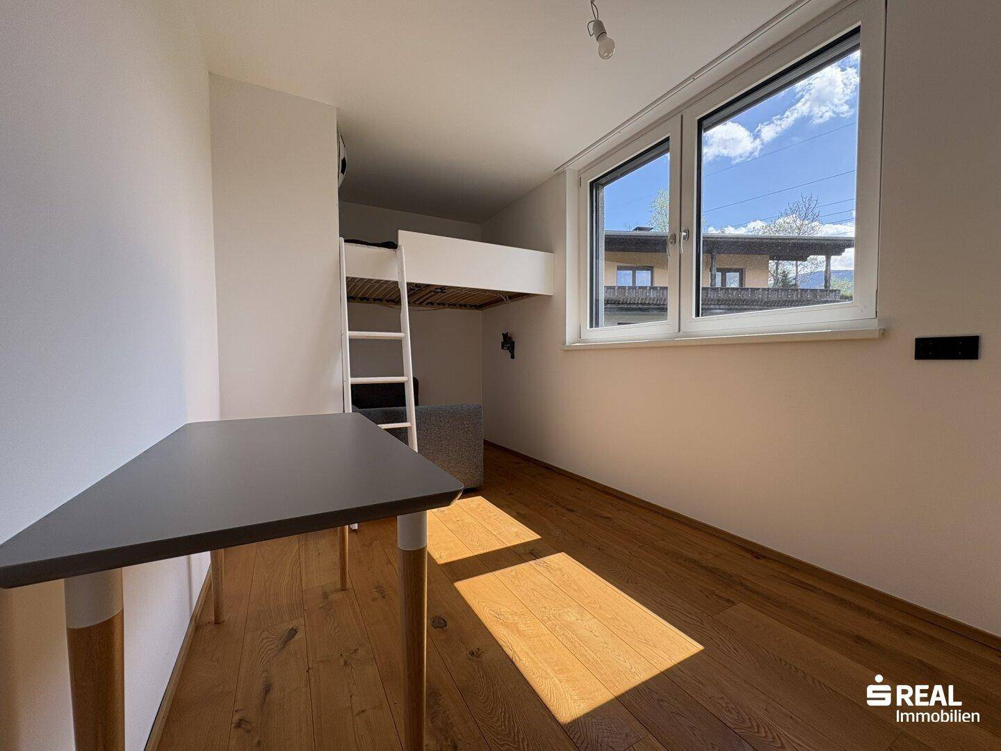 Kinderzimmer mit Hochbett, Schreibtisch und Fenster mit Blick ins Grüne.