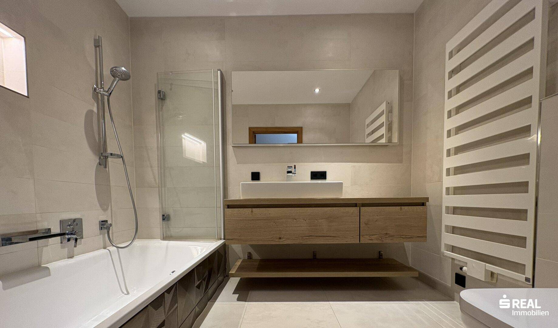 Modernes Badezimmer mit Badewanne, Dusche, Waschtisch und beheiztem Handtuchhalter.