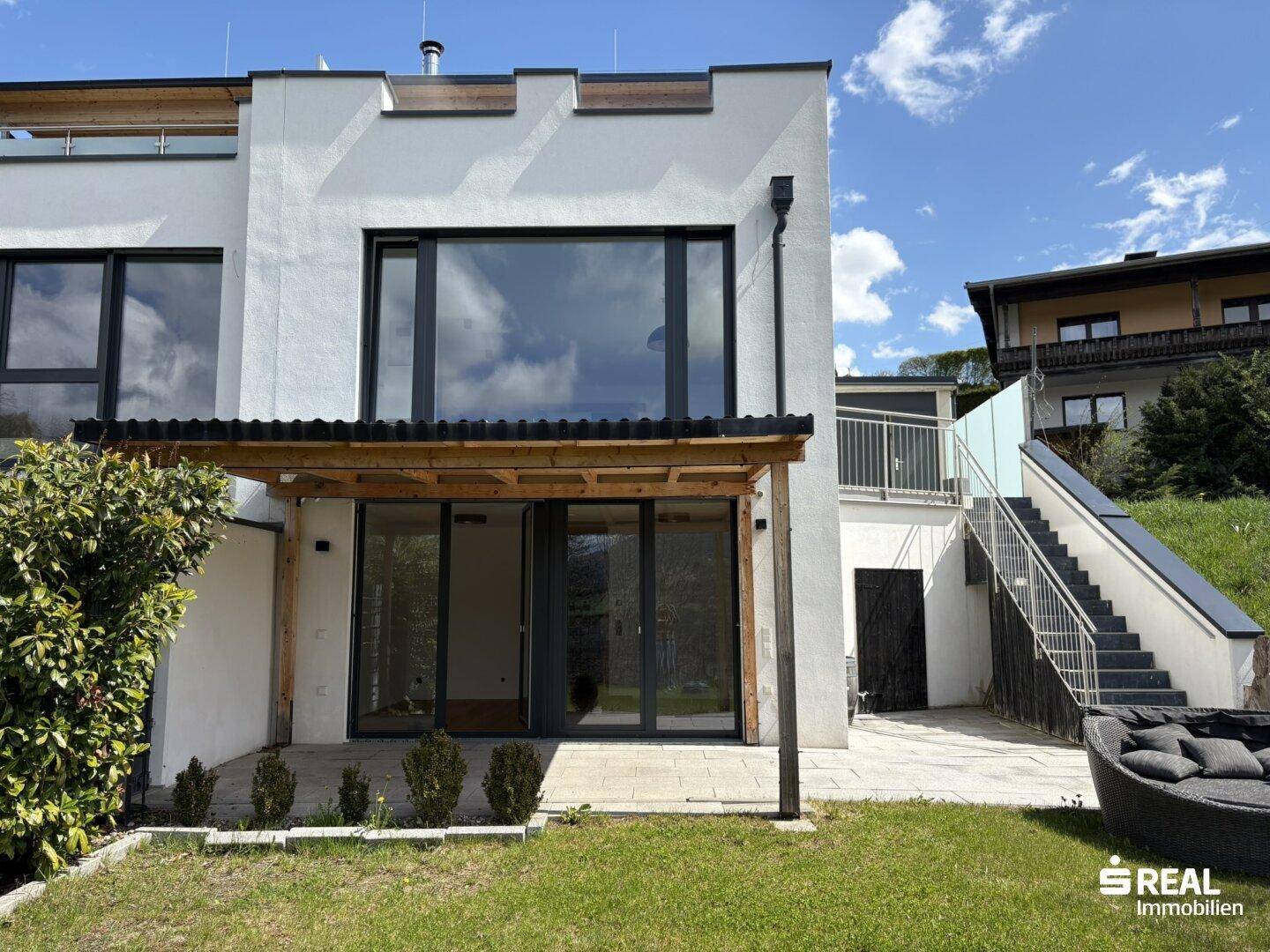 Rückansicht des modernen Hauses mit Garten, überdachter Terrasse und Außenwhirlpool.