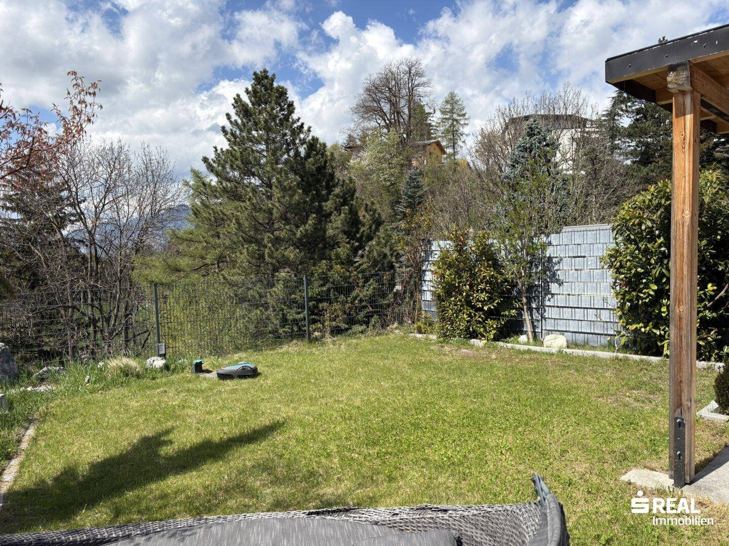 Sonniger Gartenbereich mit Rasenfläche, Bäumen und Blick in die Natur.