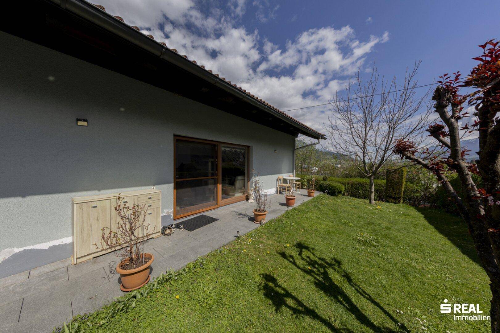 Seitenansicht des Hauses mit kleiner gepflasterter Fläche und angrenzendem Rasenbereich.
