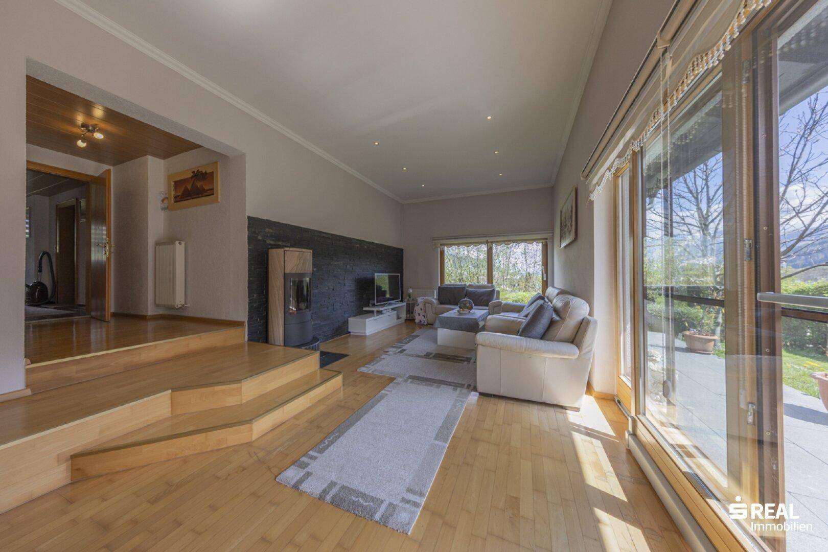 Helles Wohnzimmer mit Holzboden, großen Fenstern und Zugang zur Terrasse mit Bergblick.