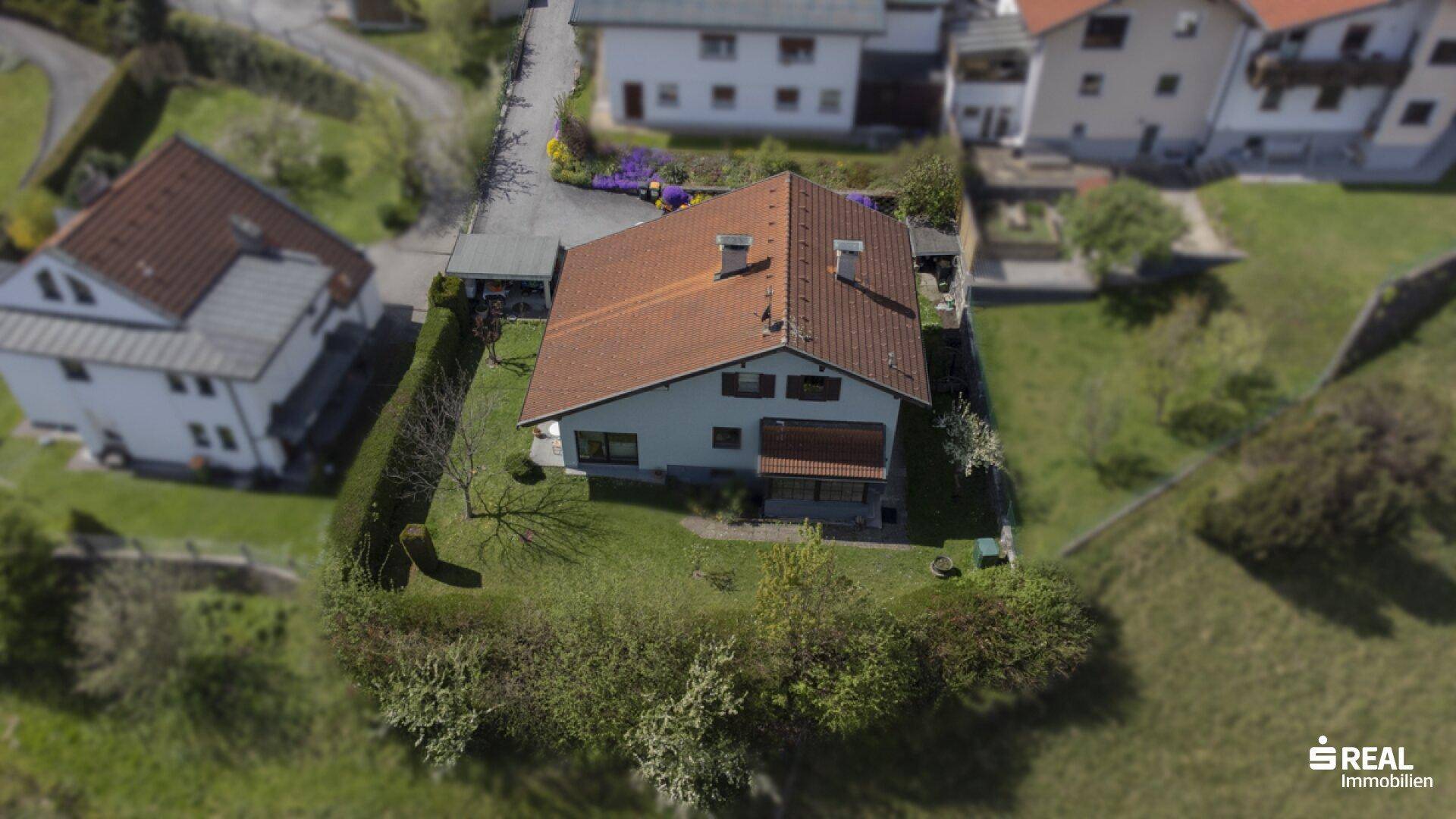 Luftaufnahme des Einfamilienhauses mit Garten und umliegender Wohnbebauung in grüner Umgebung.