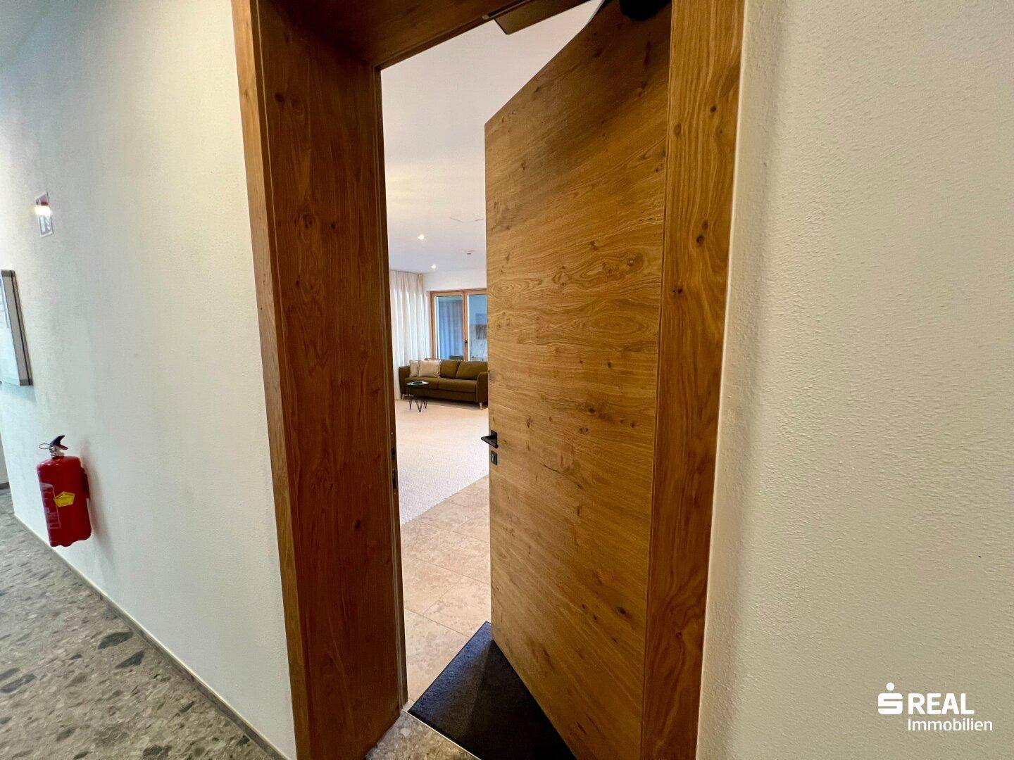 Eingangsbereich mit Holztür, Fliesenboden und Blick in den Wohnbereich.