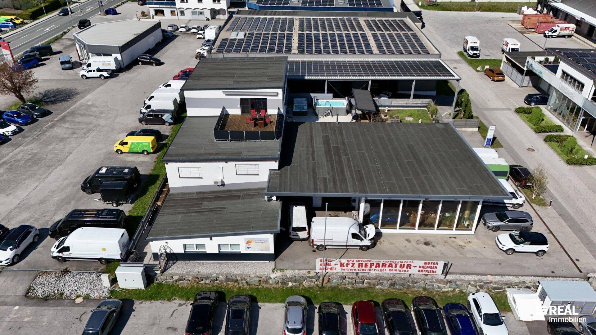 Luftaufnahme des Gebäudekomplexes mit Flachdächern, Solaranlagen und umliegenden Parkplätzen.