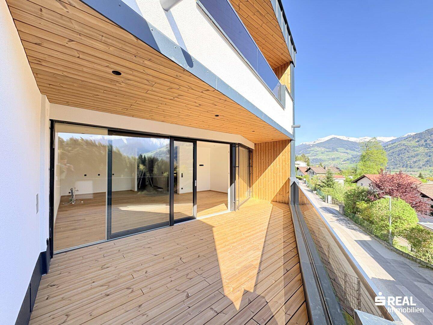 Geräumiger Holzbalkon mit Glasgeländer und weitem Blick auf die umliegende Berglandschaft.