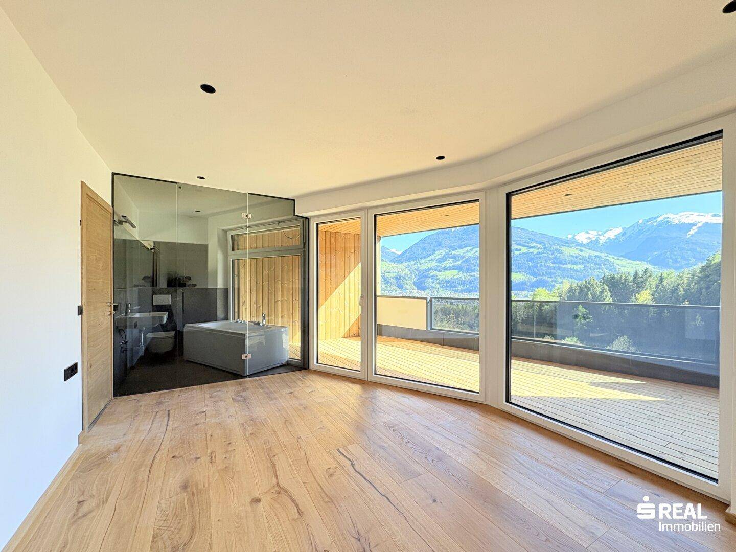 Helles Schlafzimmer mit Holzboden, integriertem Bad und Zugang zu einem großen Balkon mit Bergblick.