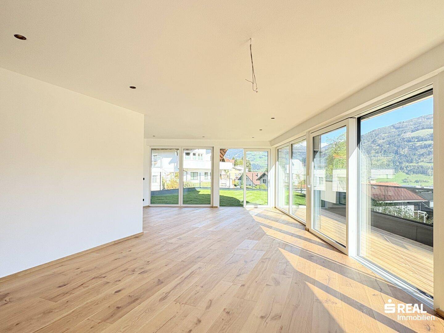 Lichtdurchfluteter Wohnbereich mit Holzboden und großen Fensterfronten, die viel Tageslicht hereinlassen.