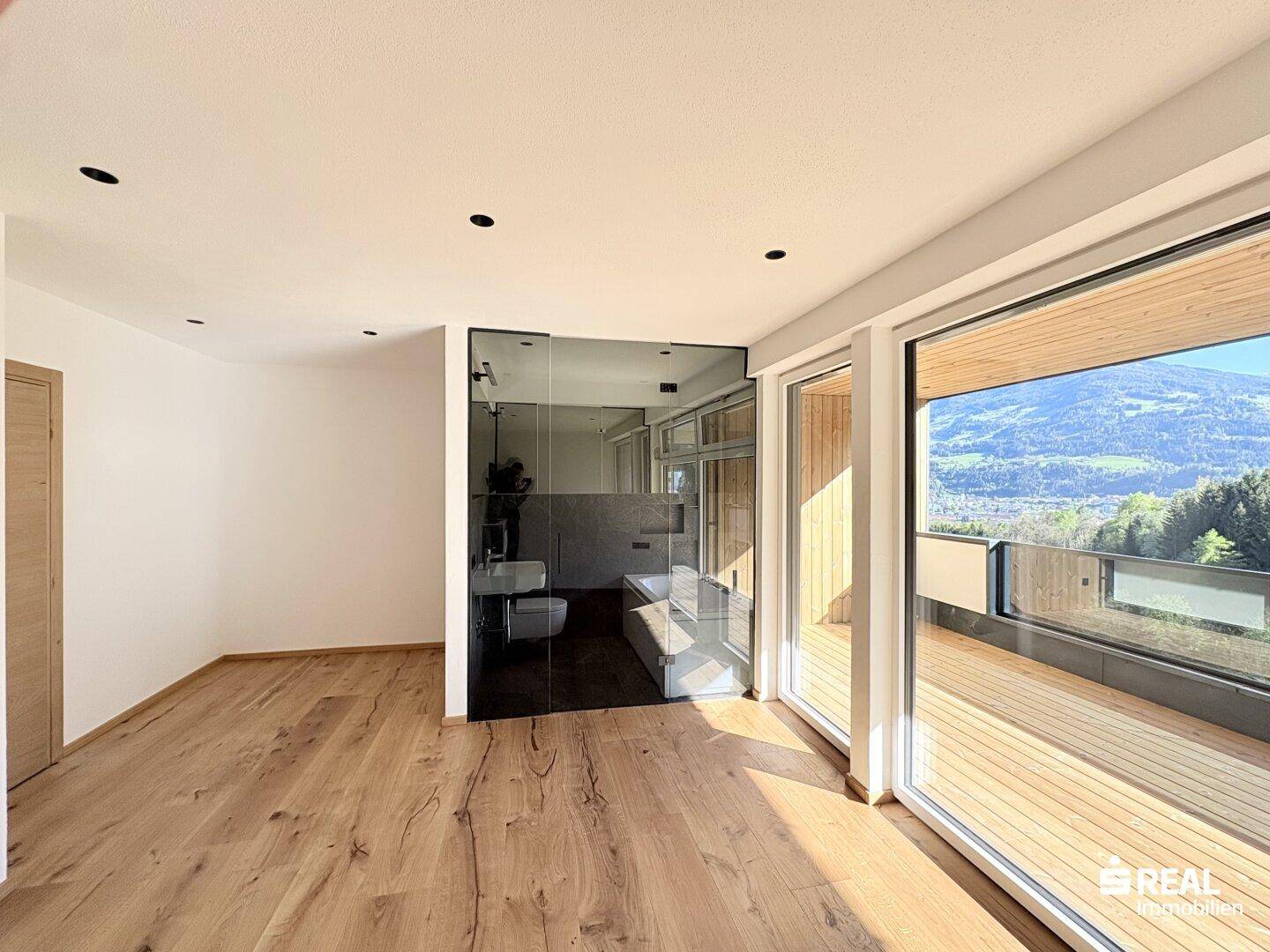 Schlafzimmer mit Holzboden, integriertem Badezimmer und Zugang zu einem Balkon mit Bergblick.