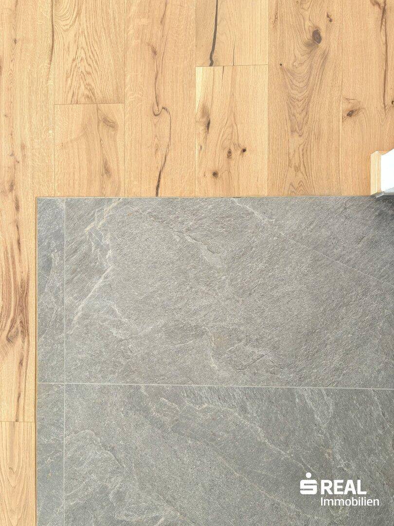 Detailaufnahme des Übergangs zwischen modernem Holzboden und eleganten grauen Fliesen.