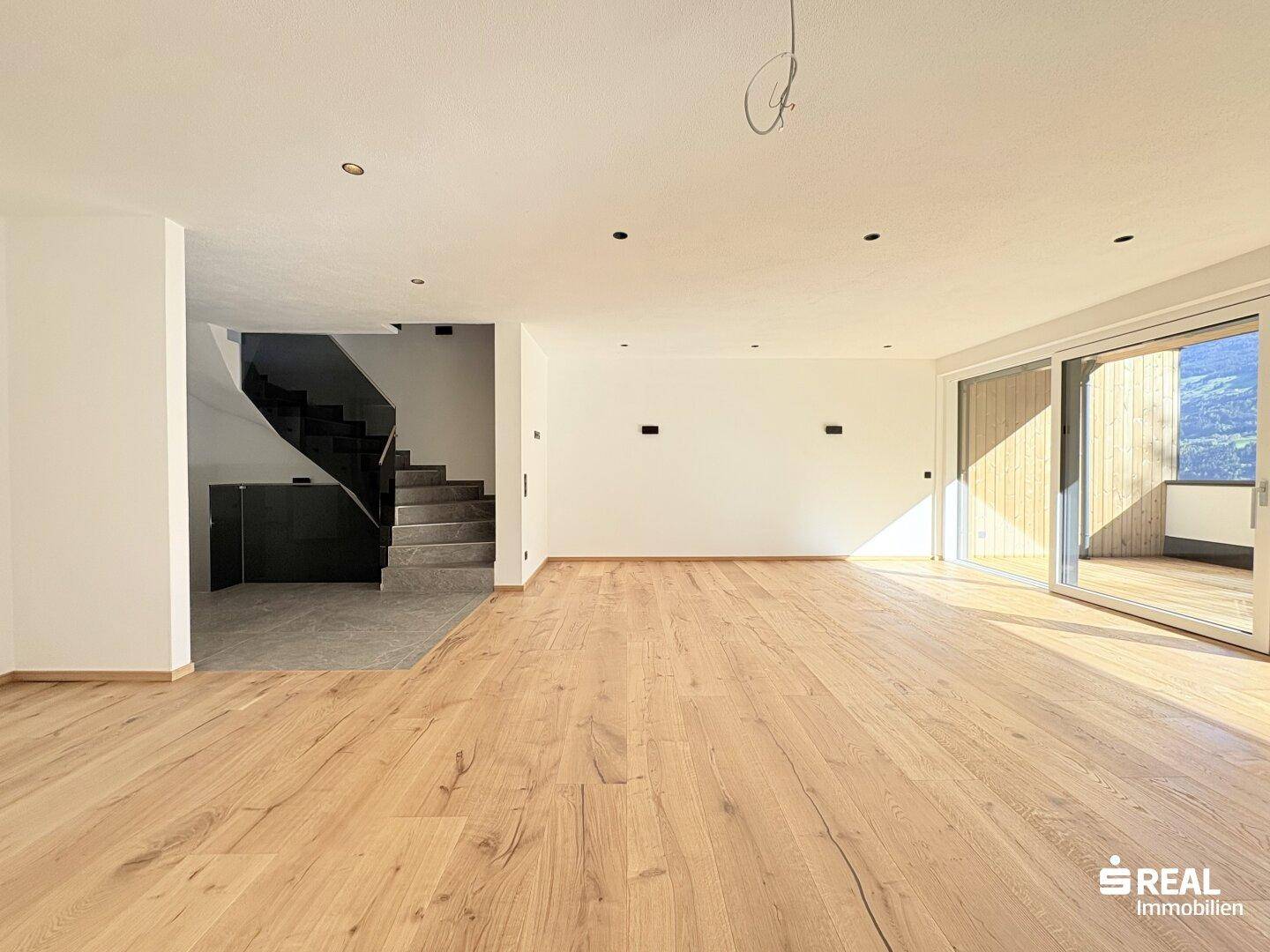 Geräumiger Wohnbereich mit Holzboden und Blick auf die moderne Treppe sowie den Außenbereich.