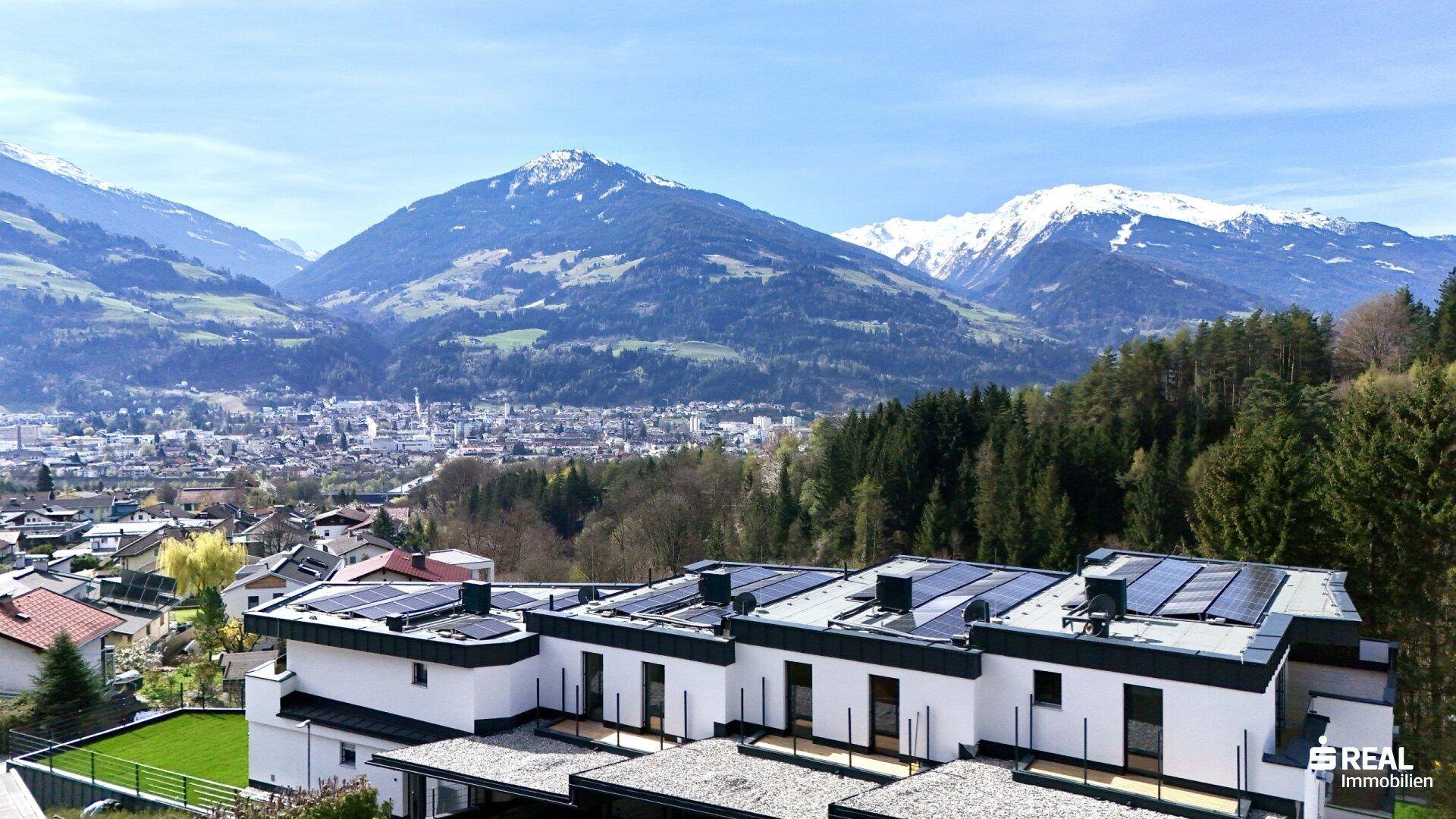 Panoramablick auf die moderne Wohnanlage mit Photovoltaikanlagen und die umliegende Bergwelt.