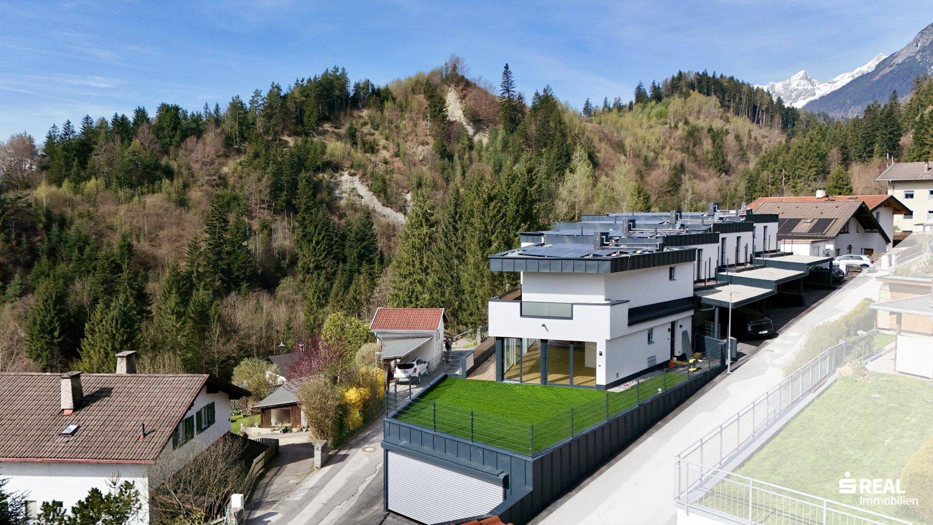 Seitenansicht der modernen Wohnanlage mit begrüntem Dachbereich und Carport in alpiner Umgebung.
