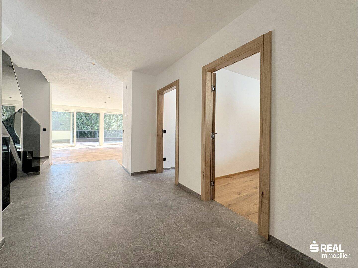 Heller Eingangsbereich mit grauen Fliesen und Holztürrahmen, offen zum Wohnbereich.