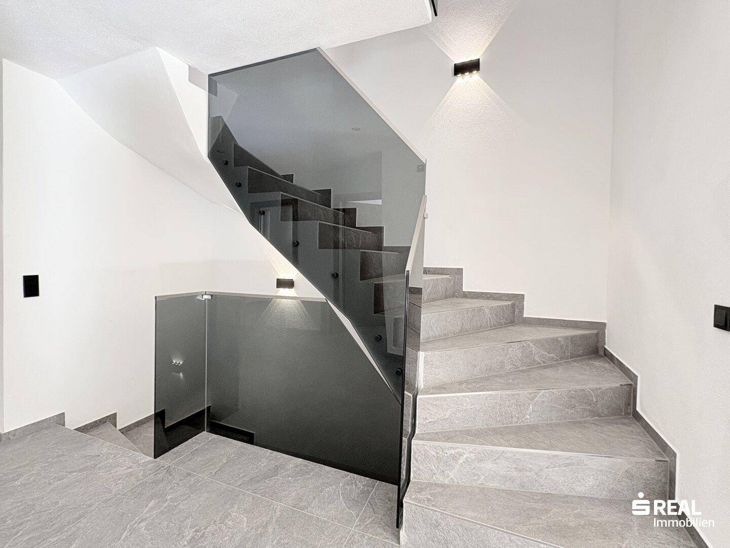 Moderne Treppe mit grauen Fliesenstufen und eleganter Glasbrüstung.