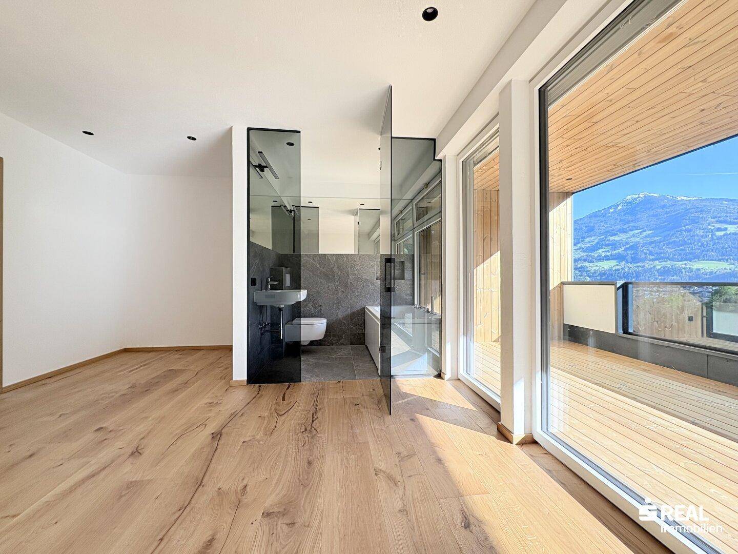 Geräumiges Schlafzimmer mit Holzboden, Zugang zum Balkon und integriertem Bad.
