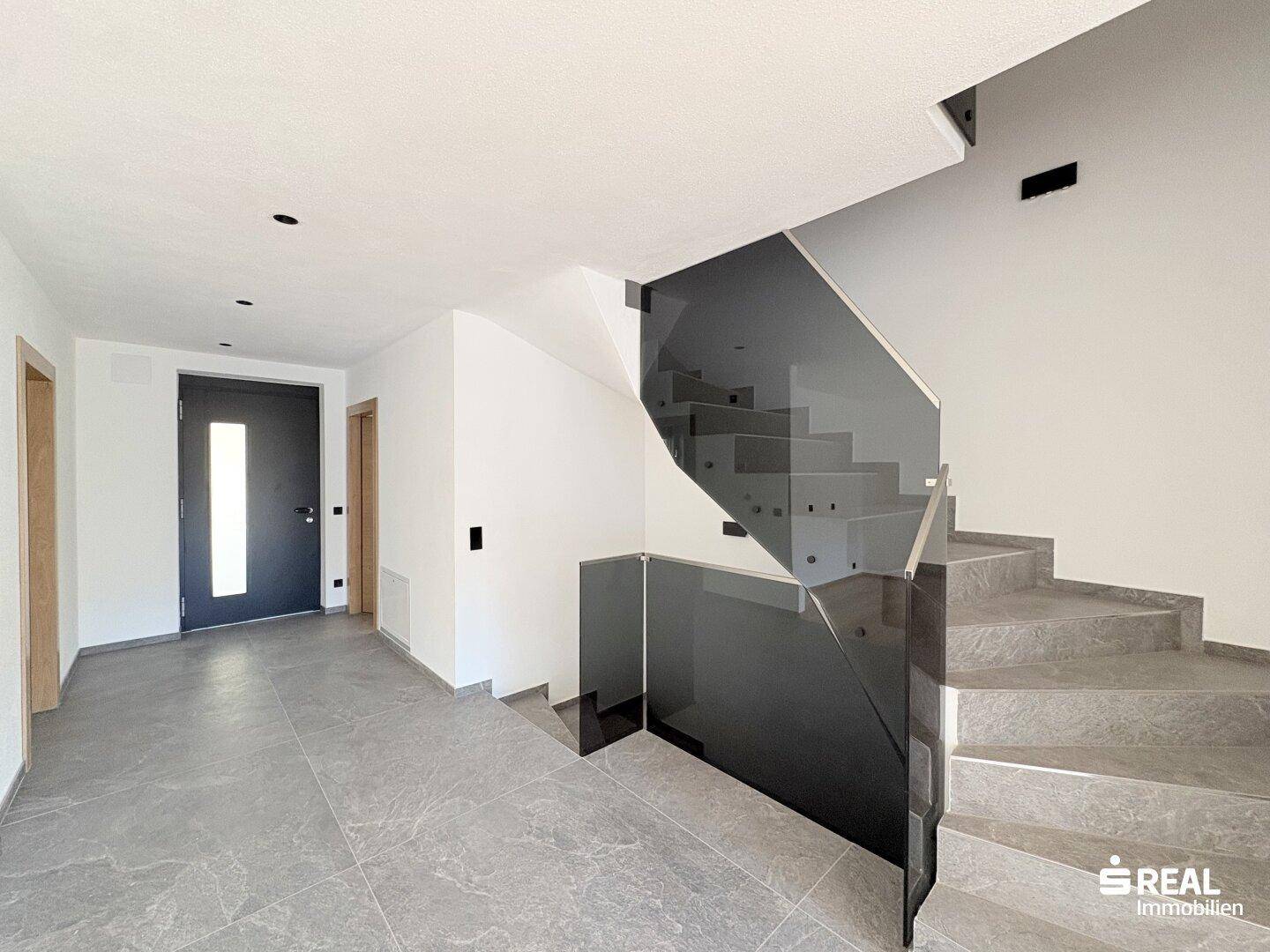 Moderner Eingangsbereich mit Treppe, Glasgeländer und dunkler Eingangstür.
