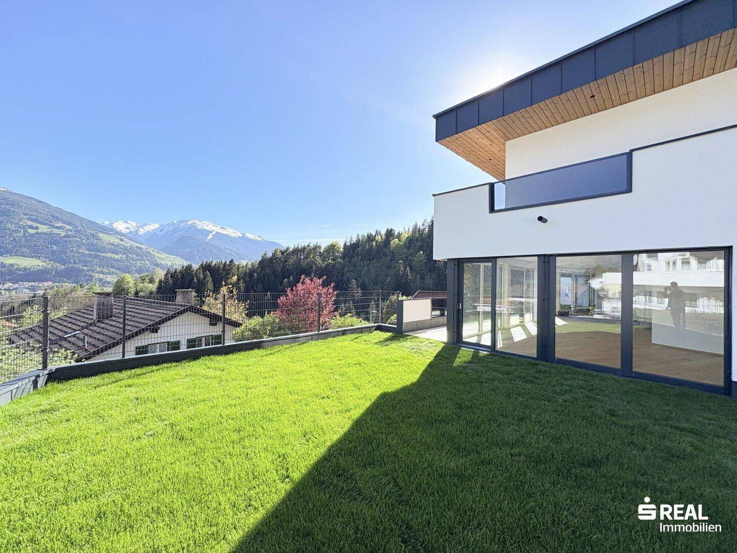 Sonnige Rasenfläche vor der modernen Fassade mit beeindruckendem Bergblick.