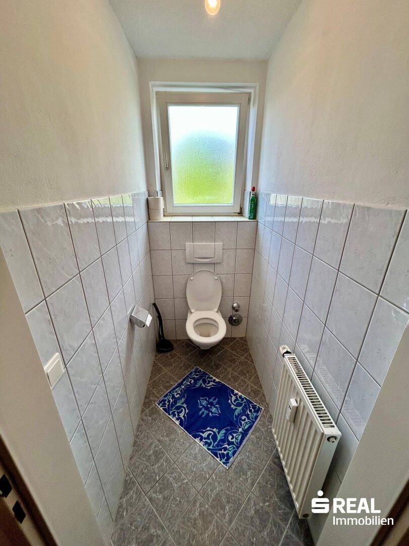 Separates WC mit Fenster, Toilette und Fliesen an den Wänden.