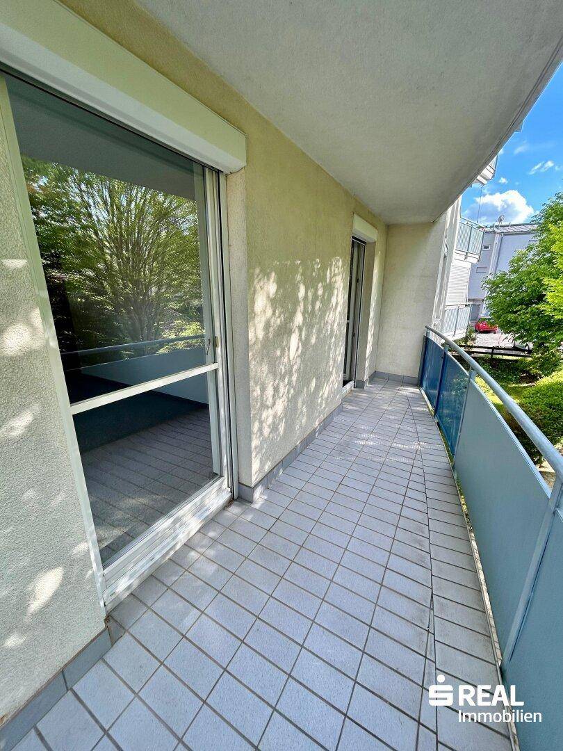 Langer Balkon mit Fliesenboden und Blick auf die grüne Umgebung.