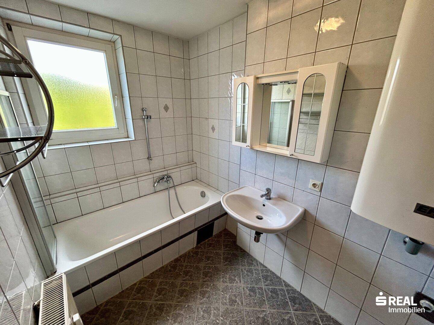 Helles Badezimmer mit Badewanne, Waschbecken, Spiegelschrank und Fenster.