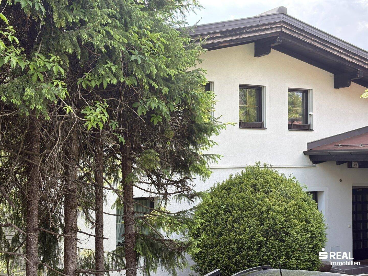 Detailansicht der Hausfassade mit Fenstern und umgebenden Bäumen.