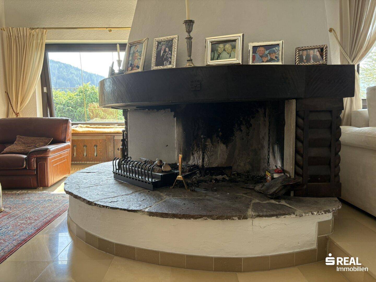 Detailaufnahme des großen Kamins im Wohnzimmer, umgeben von Fenstern mit Bergblick.
