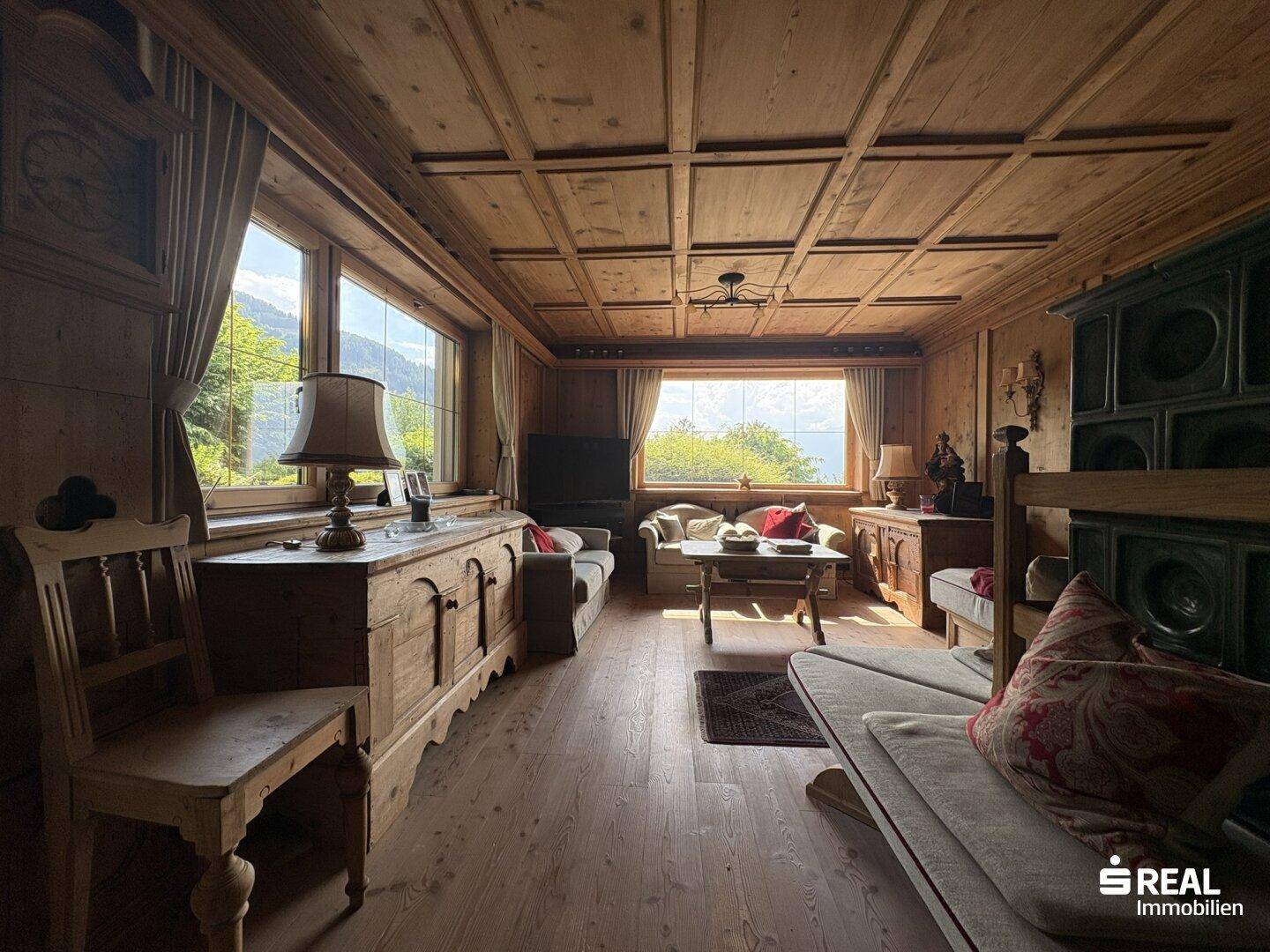 Gemütliches Wohnzimmer im alpinen Stil mit Holztäfelung, Kachelofen und Bergblick.