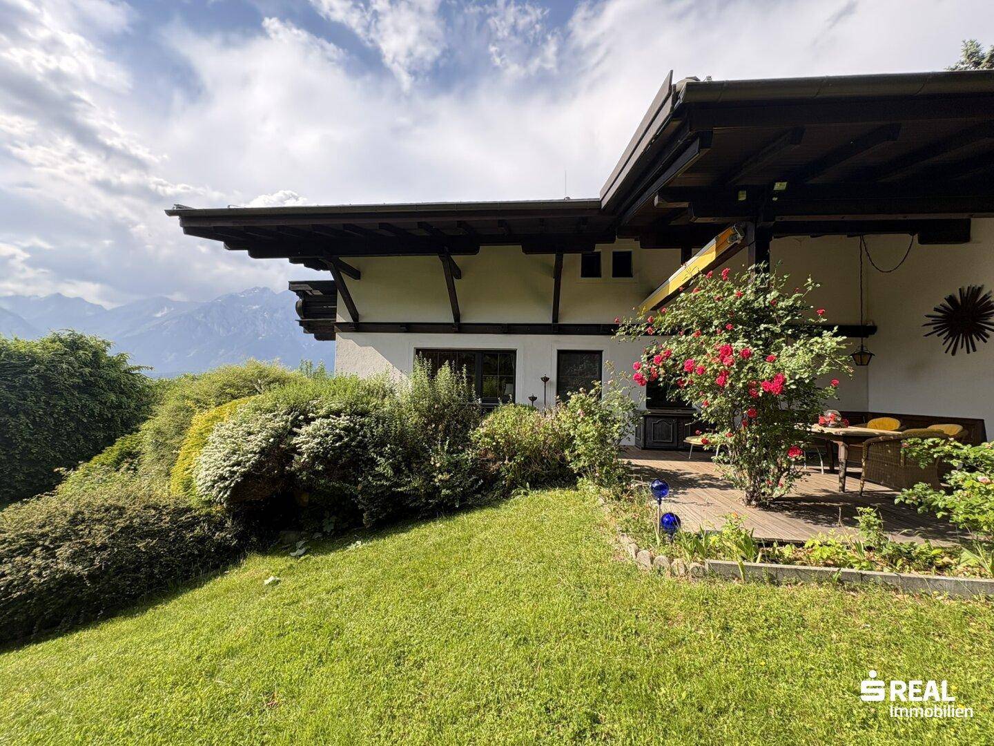 Gemütliche Terrasse mit Sitzgelegenheiten und Rosenbusch, umgeben von einem gepflegten Garten mit Bergblick.
