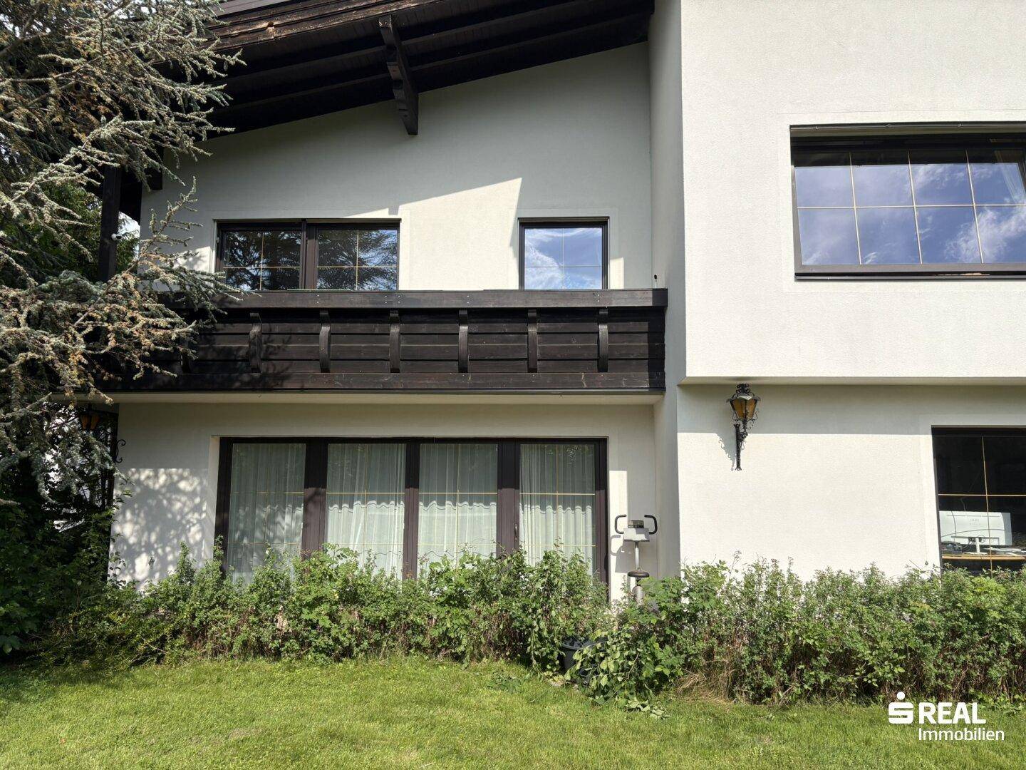 Nahaufnahme der Hausfassade mit Balkon und üppiger Bepflanzung im Vordergrund.