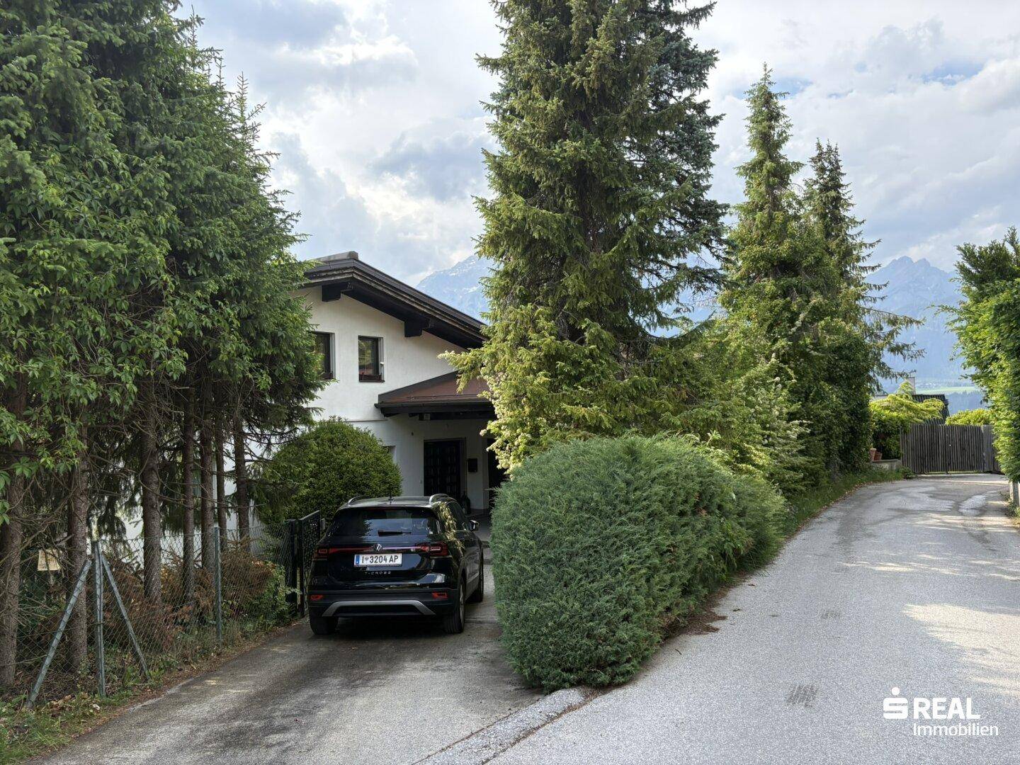 Zufahrt zum Anwesen mit geparktem Auto und Blick auf die Berge im Hintergrund.