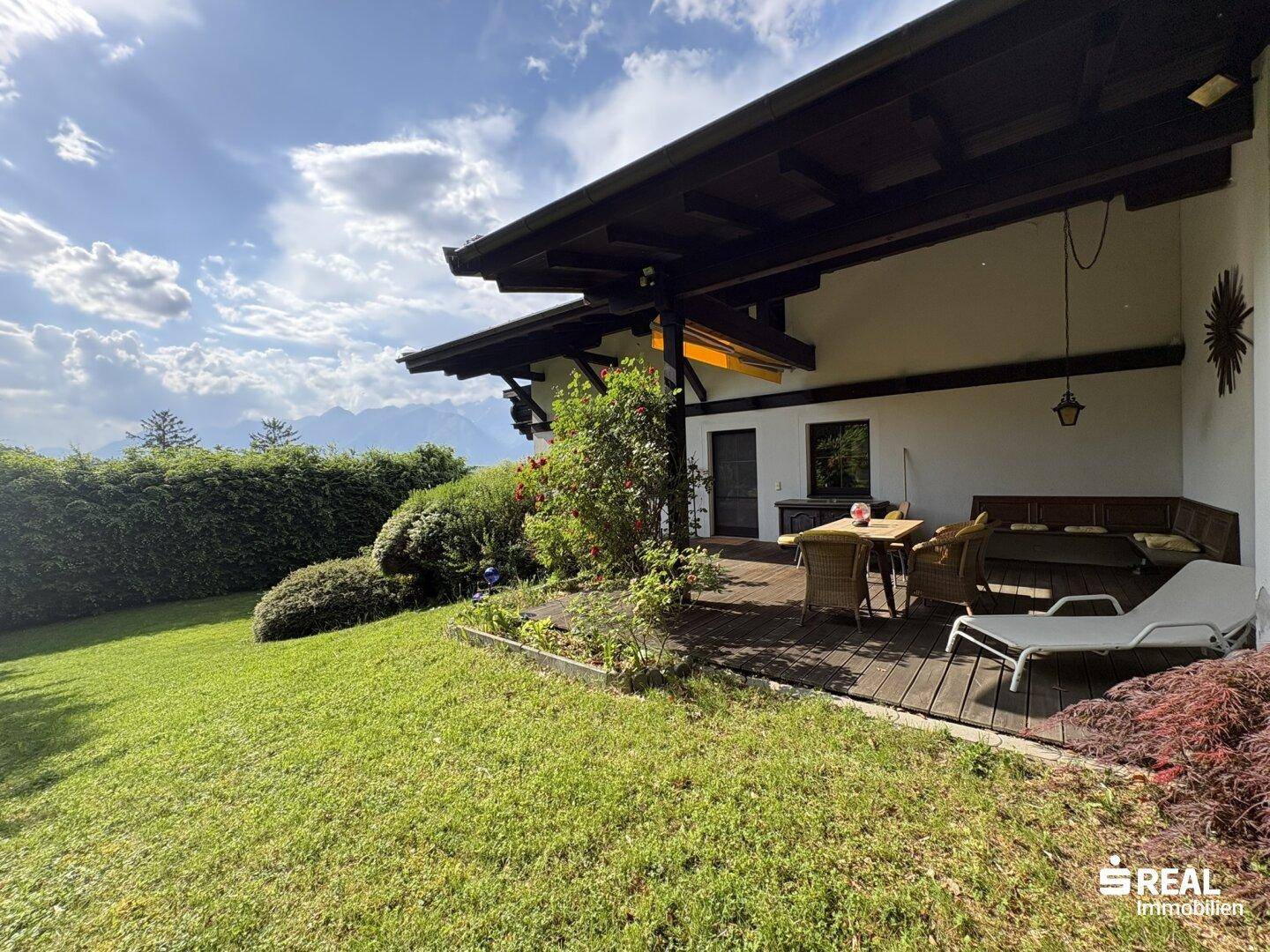 Sonnige Terrasse mit Holzdeck, Gartenmöbeln und Zugang zum gepflegten Rasen.