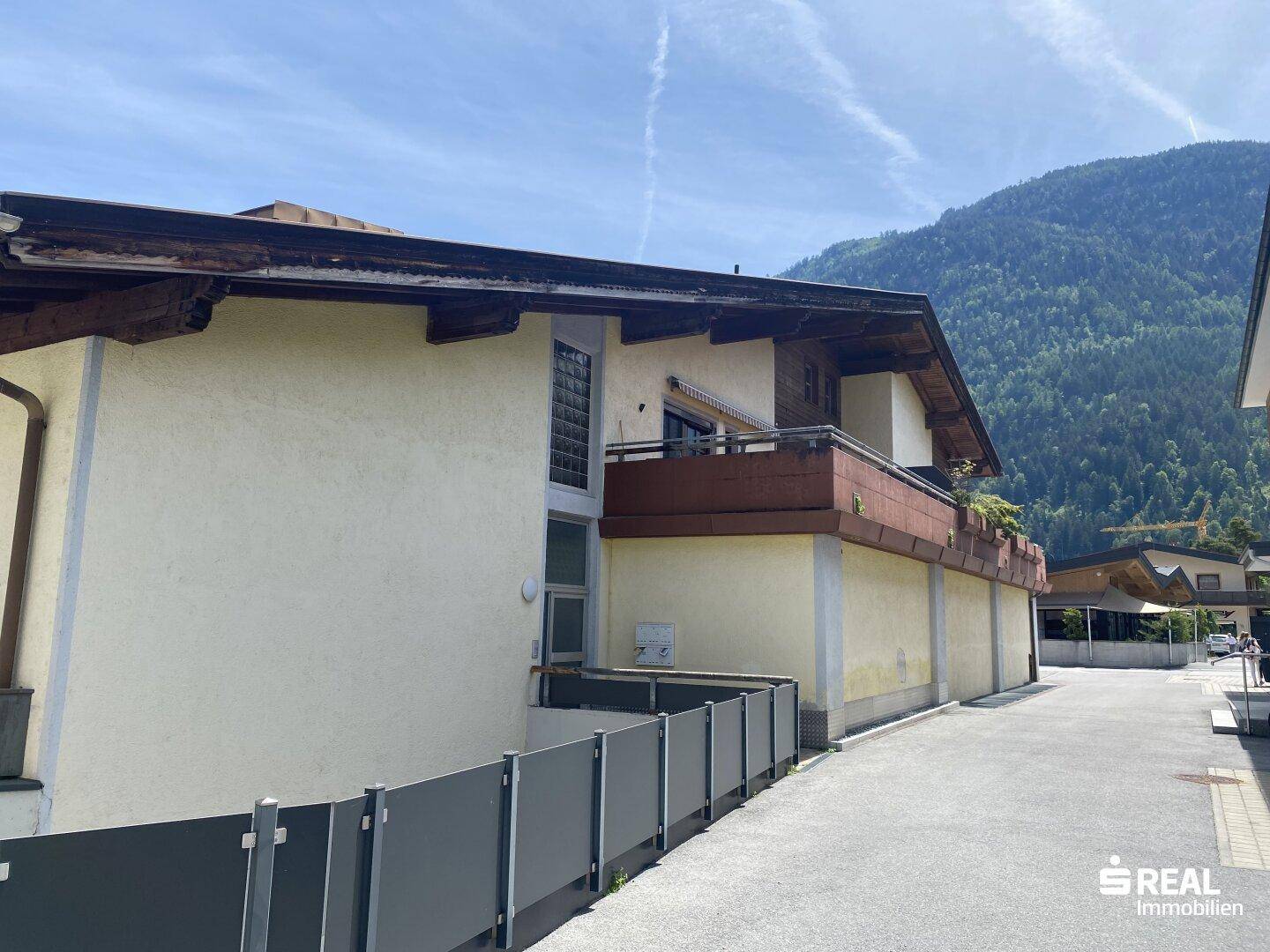 Seitenansicht des Gebäudes mit Balkon und Blick auf die umliegende Berglandschaft unter klarem Himmel.