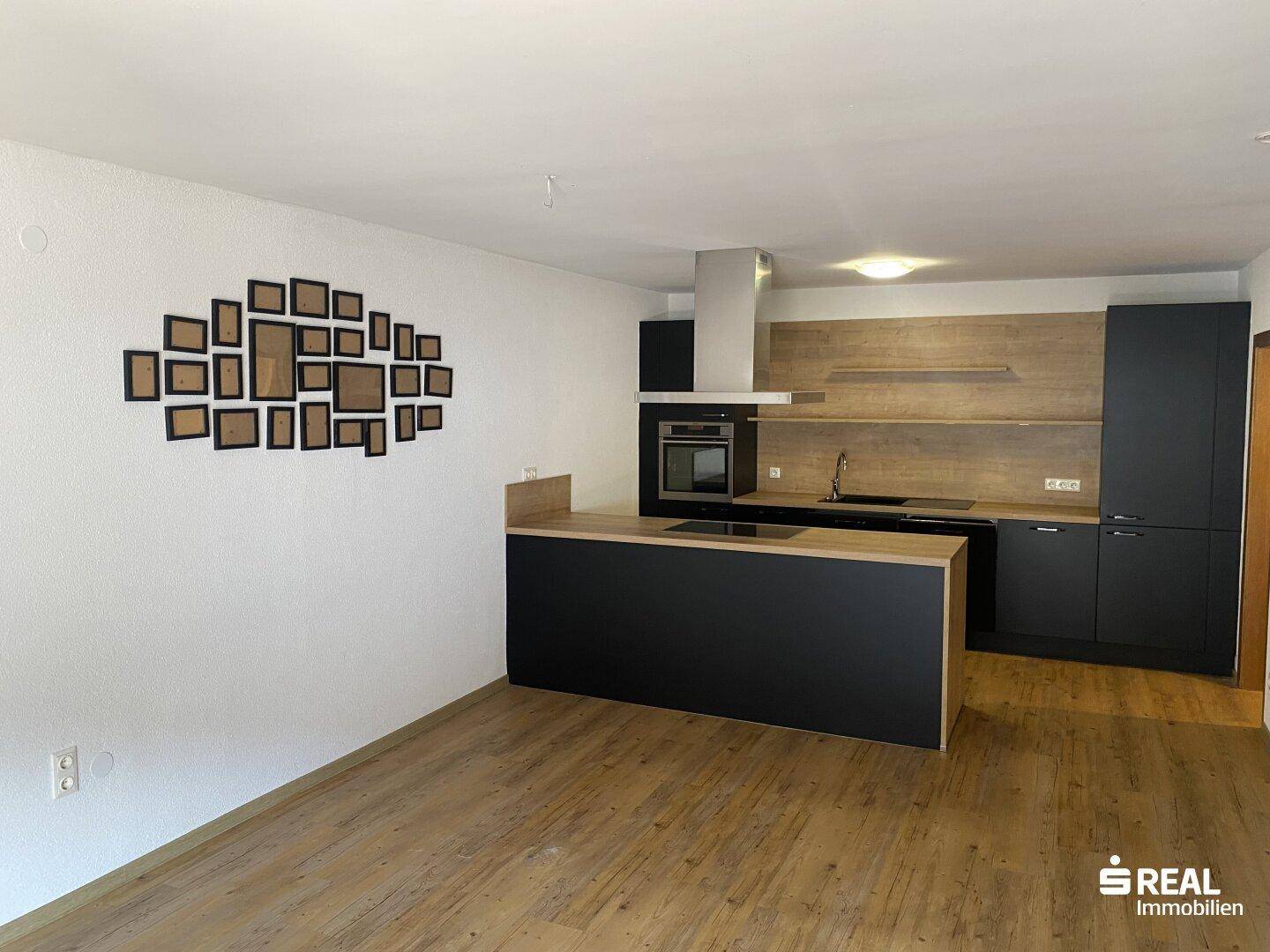 Moderne offene Küche mit schwarzen Fronten, Holzarbeitsplatte und Laminatboden im Wohnbereich.