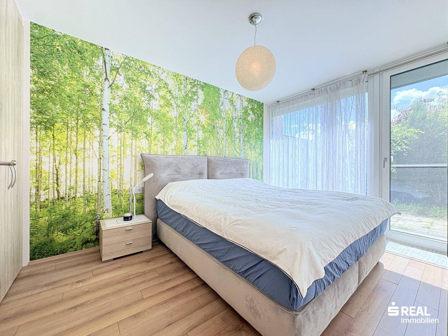 Helles Schlafzimmer mit Holzboden, großer Fensterfront und dekorativer Waldtapete.