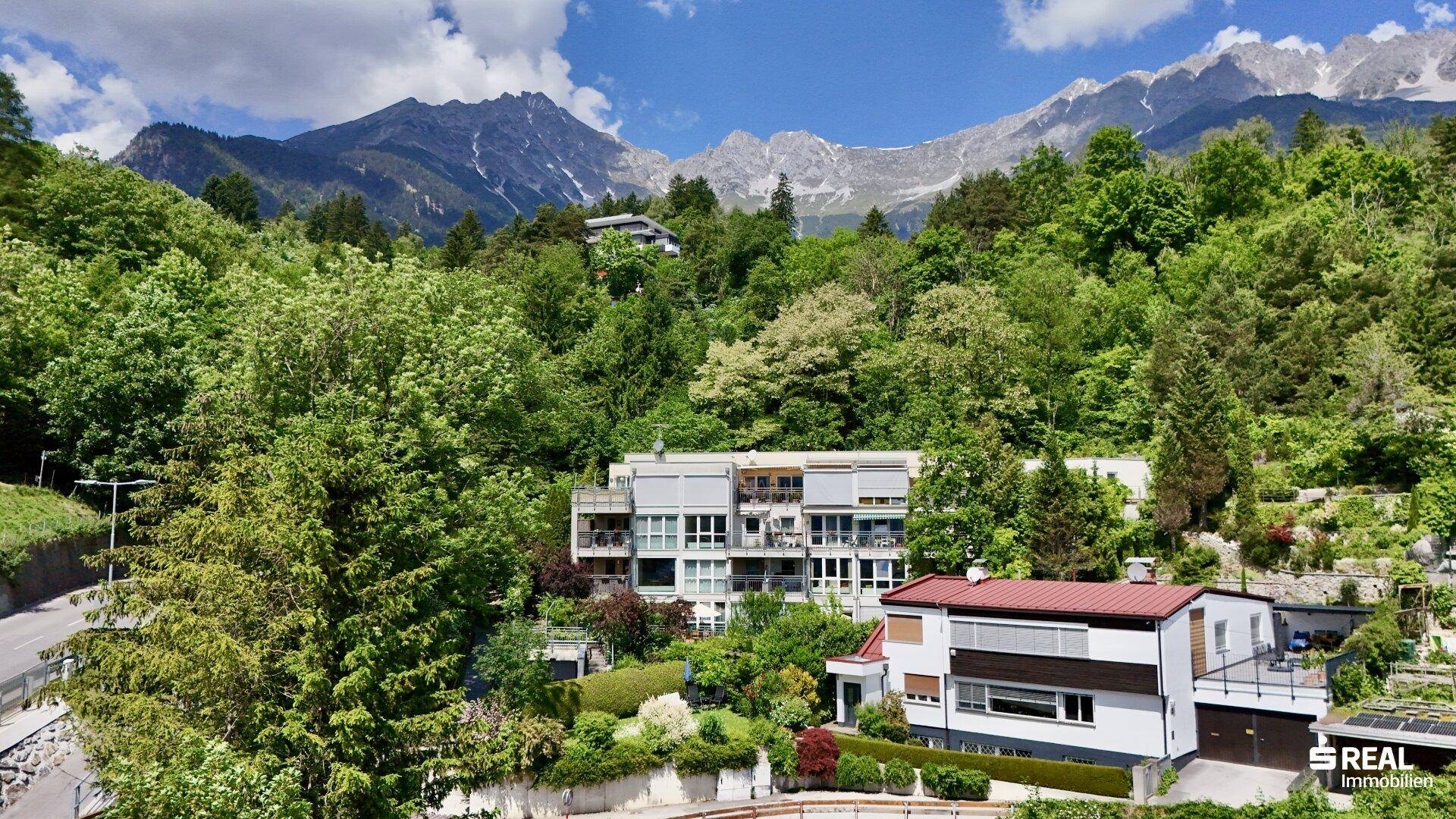 Modernes Wohngebäude eingebettet in eine grüne Hanglage mit Bergblick.