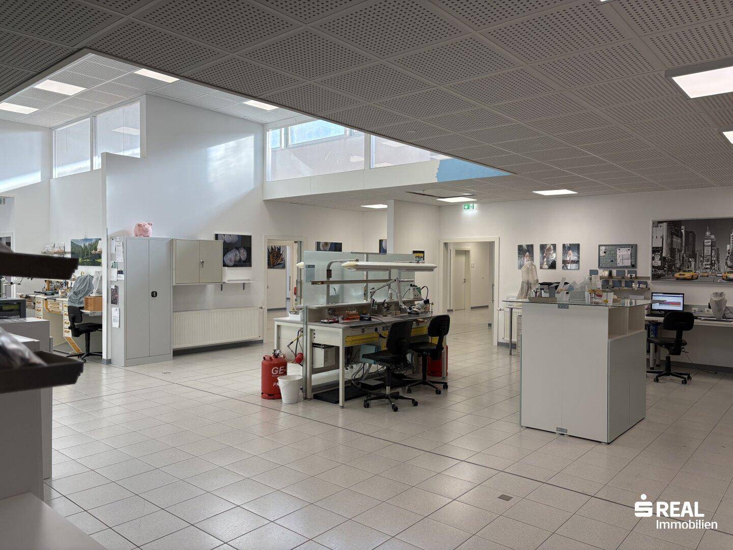 Großer, heller Arbeitsbereich mit Fliesenboden, perforierter Decke und viel Tageslicht durch Oberlichter.