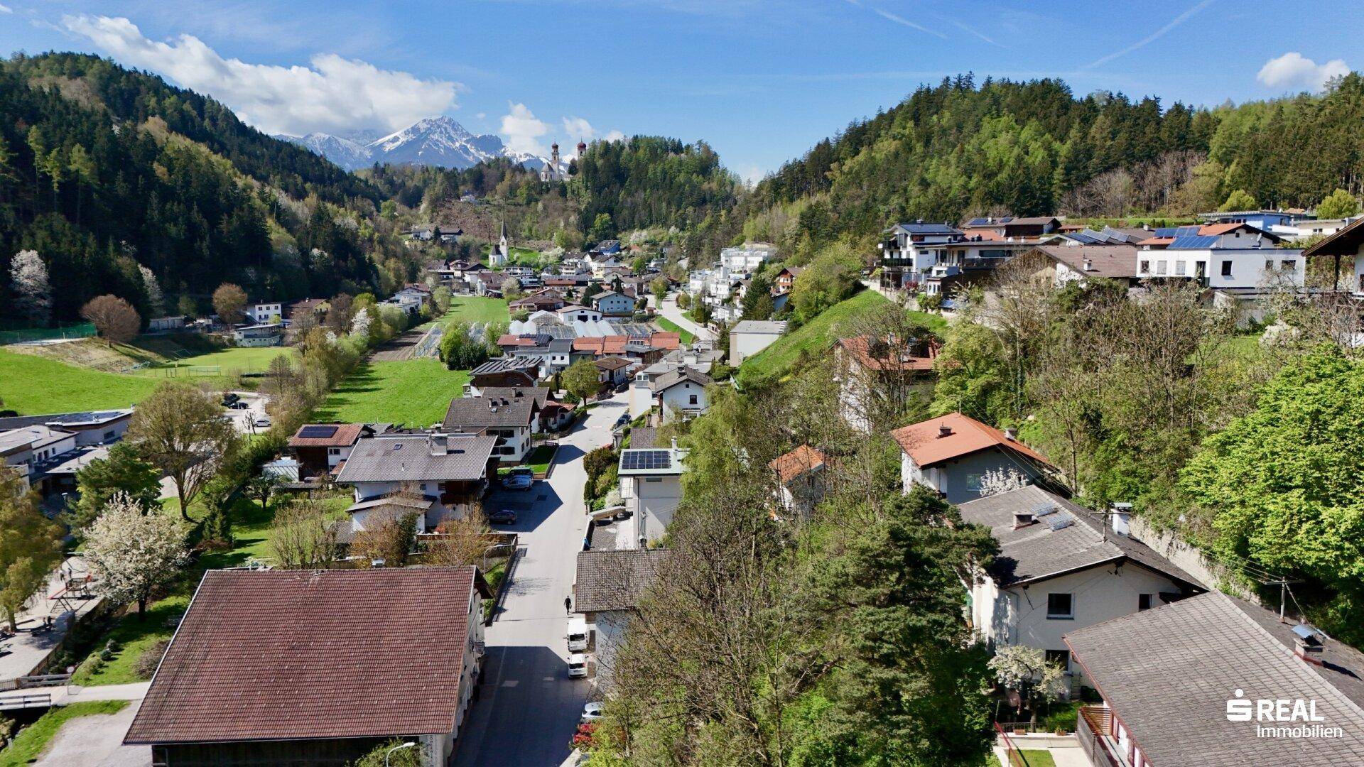 Weitläufige Luftaufnahme eines malerischen Dorfes eingebettet in eine grüne Hügellandschaft mit Bergen.