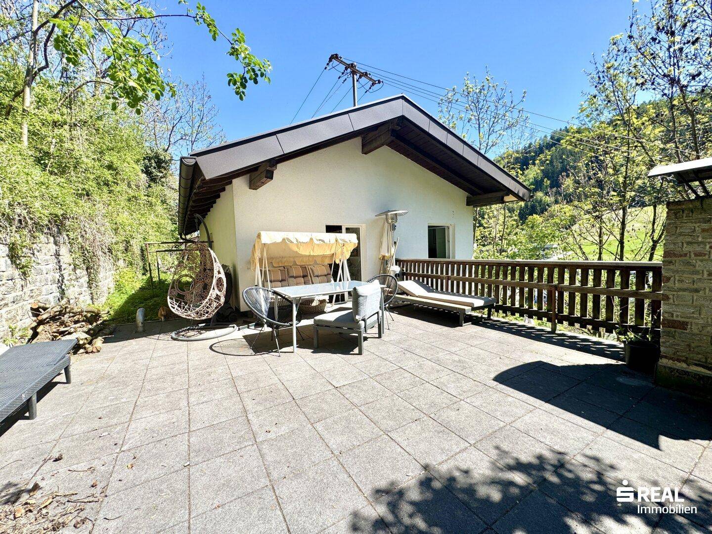 Geräumige Terrasse mit Fliesenboden und Gartenmöbeln, umgeben von grüner Natur.