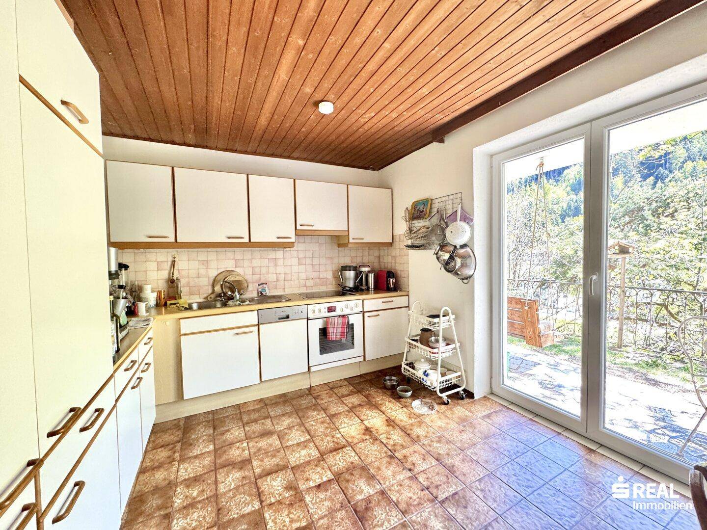 Funktionale Küche mit Holzdecke, Fliesenboden und Zugang zu einem Außenbereich.