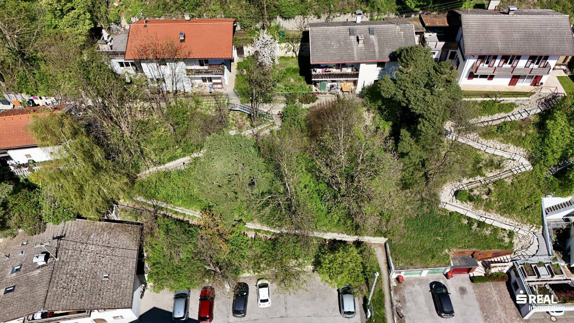 Luftaufnahme des Grundstücks mit zwei Häusern und umliegender Vegetation sowie Parkplätzen.