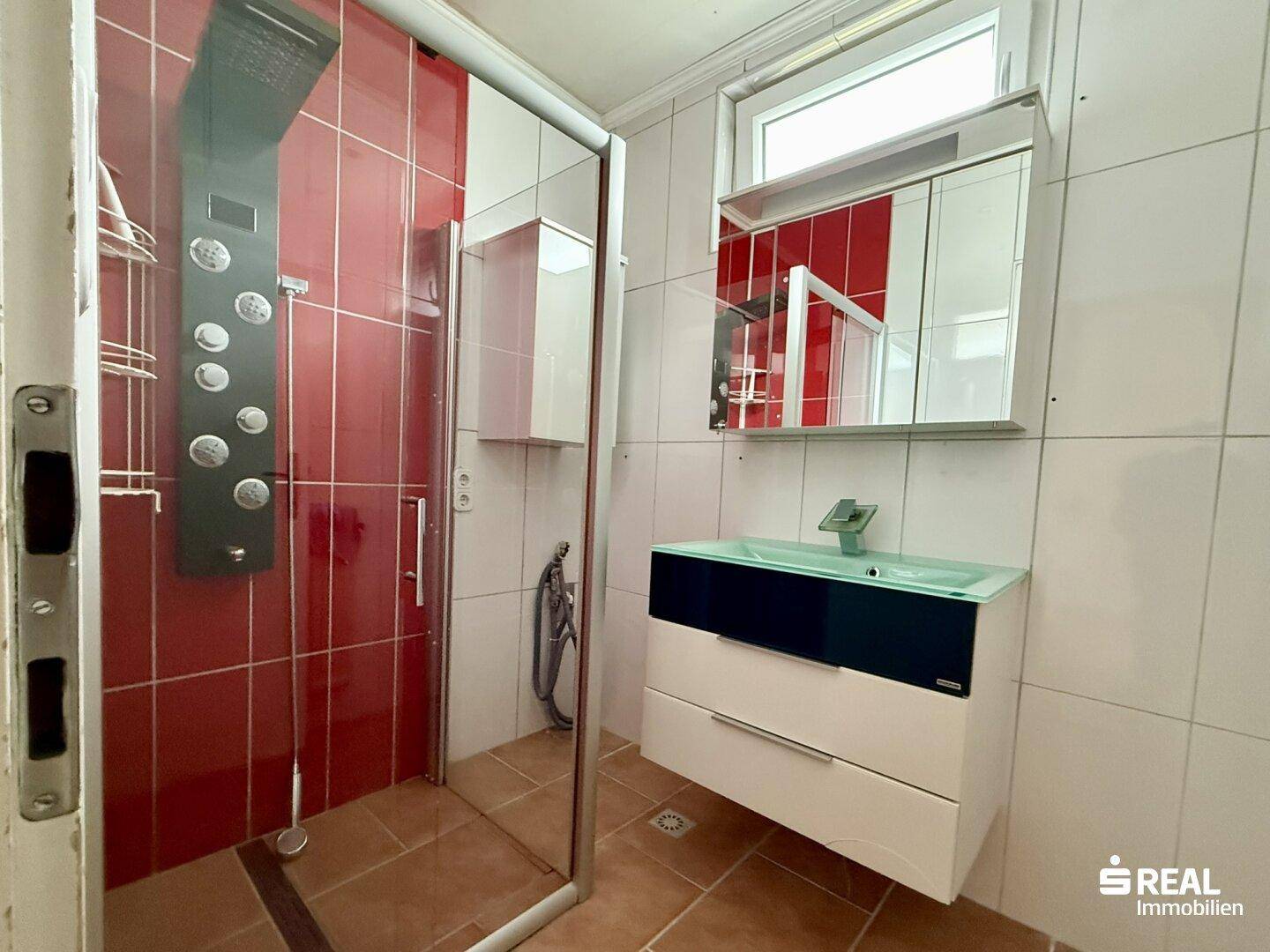 Modernes Badezimmer mit roten und weißen Fliesen, Duschkabine und einem Waschtisch mit Spiegelschrank.